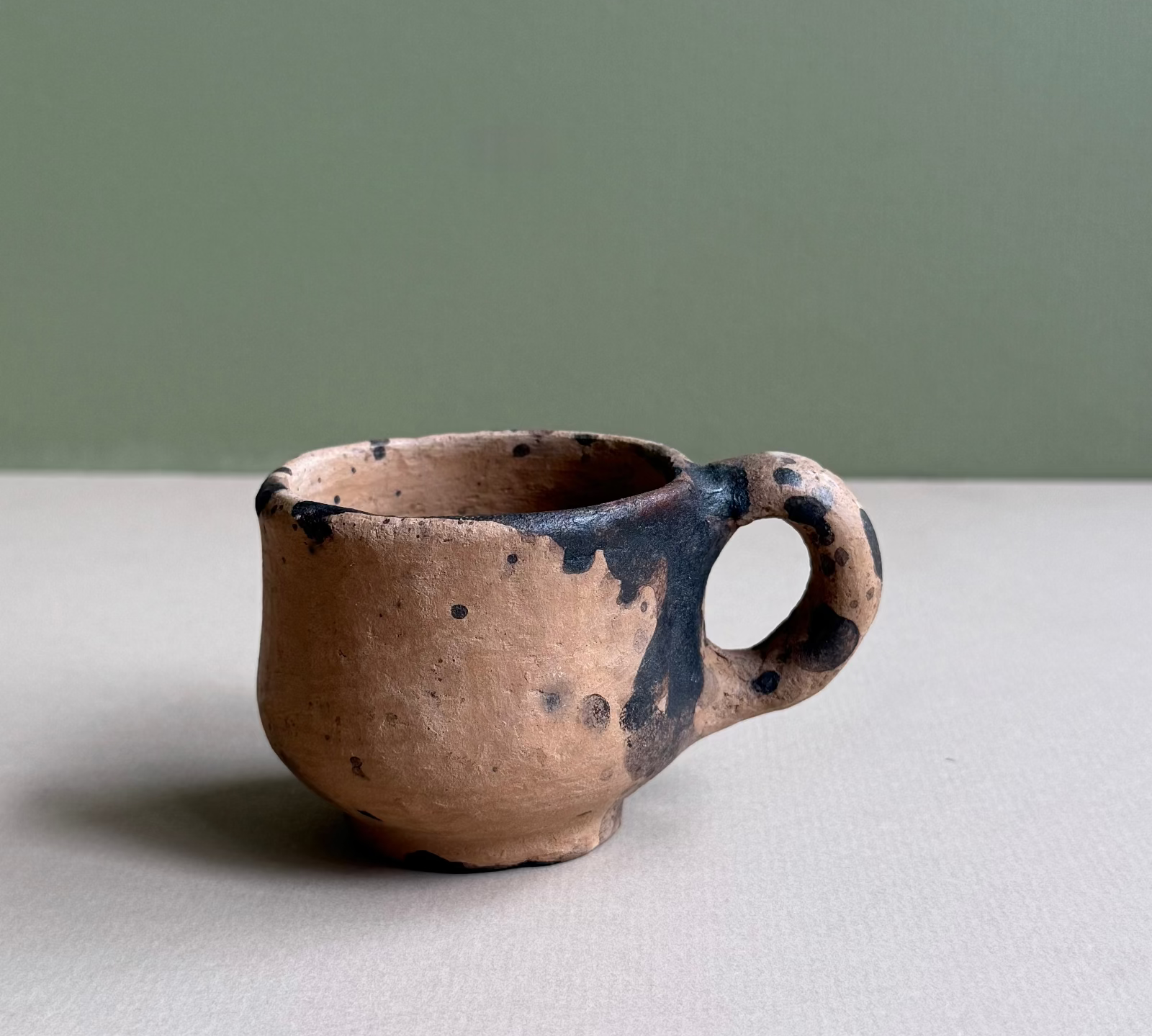 Small ceramic cup with black speckles on a neutral background