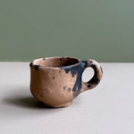 Small ceramic cup with black speckles on a neutral background