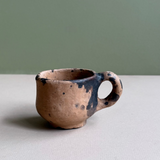 Small ceramic cup with black speckles on a neutral background
