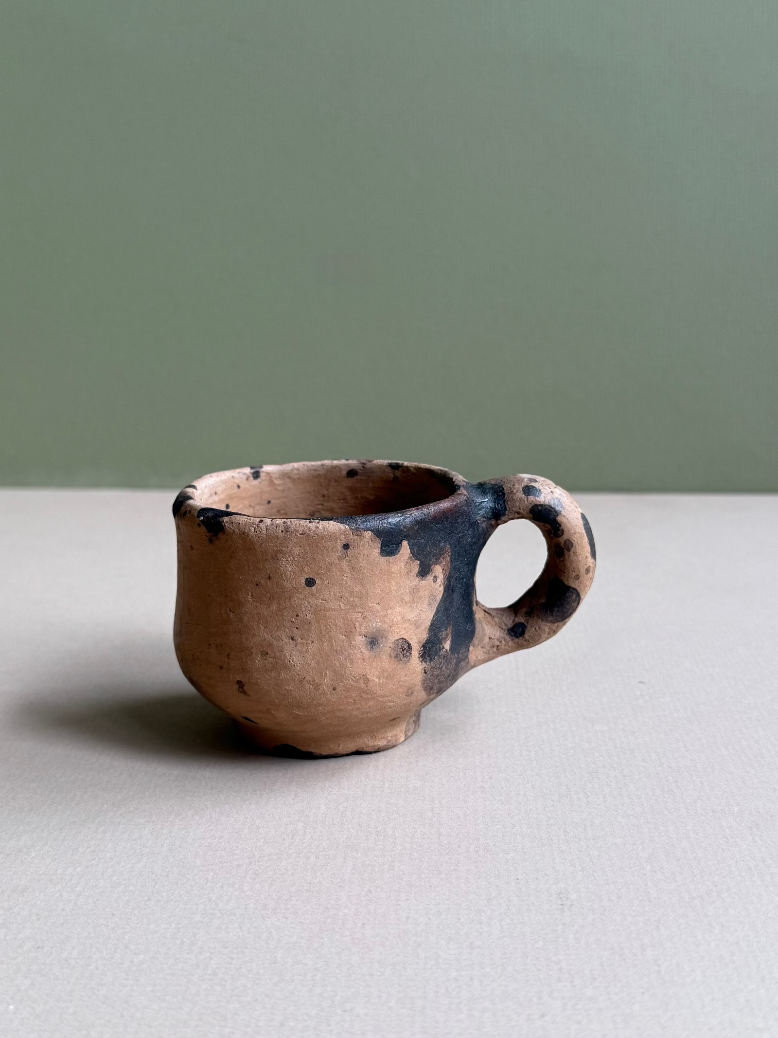 Small ceramic cup with black speckles on a neutral background
