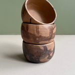 Stack of three wooden bowls with natural patterns on a light surface and green background