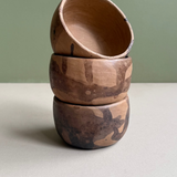 Stack of three wooden bowls with natural patterns on a light surface and green background
