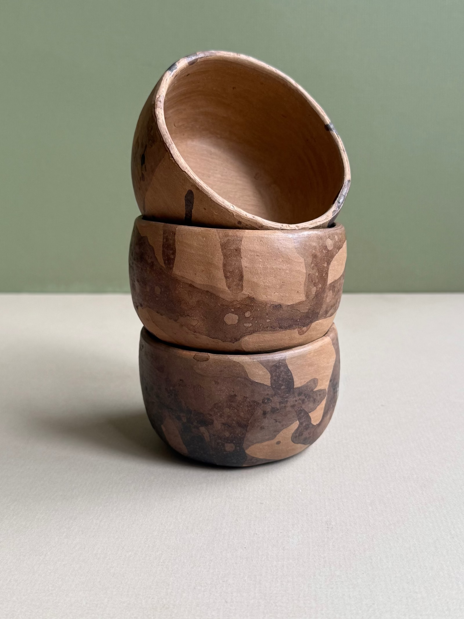 Stack of three wooden bowls with natural patterns on a light surface and green background