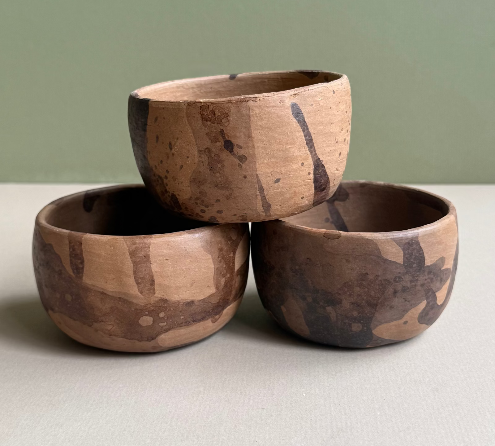 Three wooden bowls stacked on a light surface with a green background