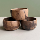 Three wooden bowls stacked on a light surface with a green background
