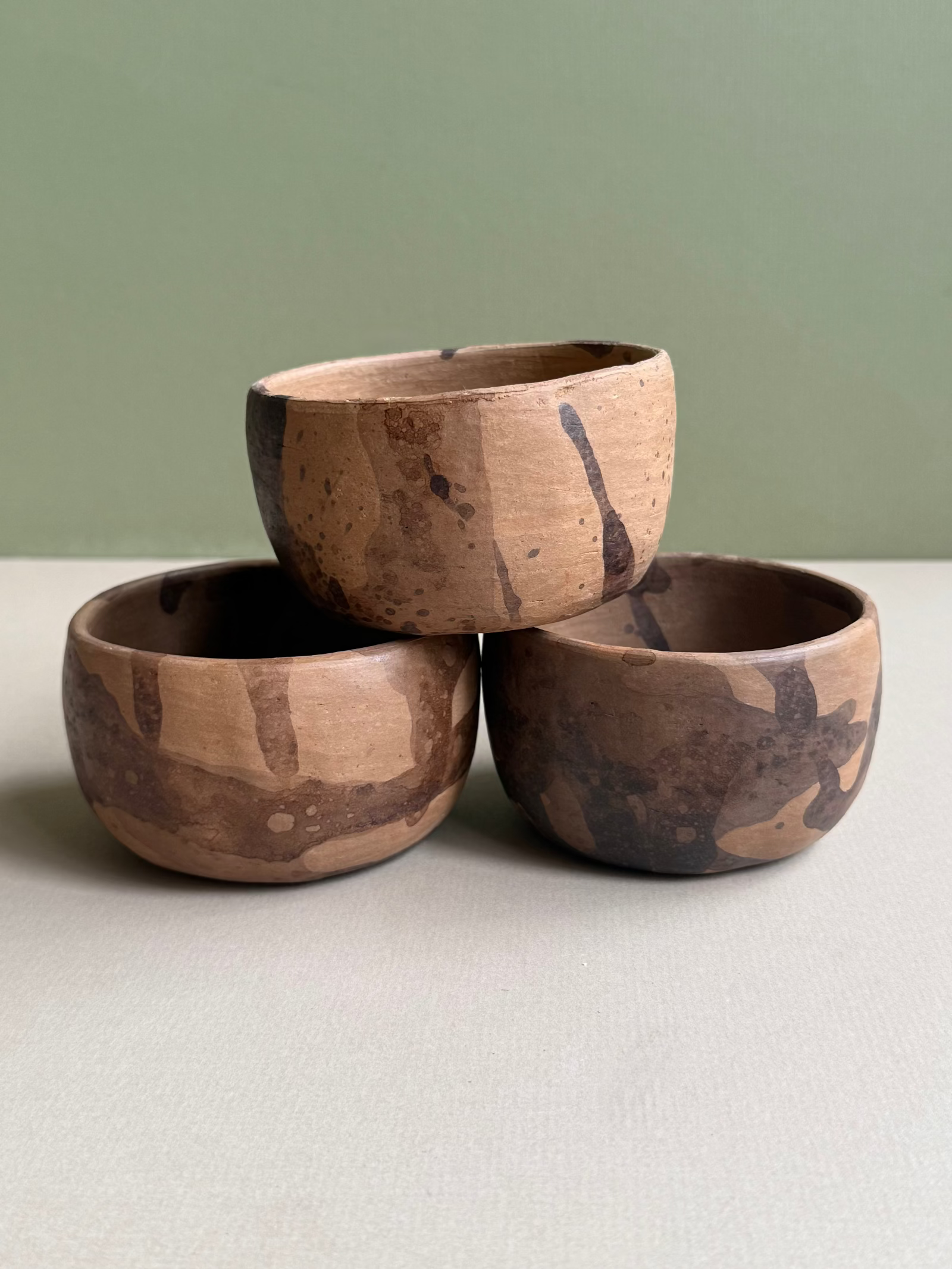 Three wooden bowls stacked on a light surface with a green background